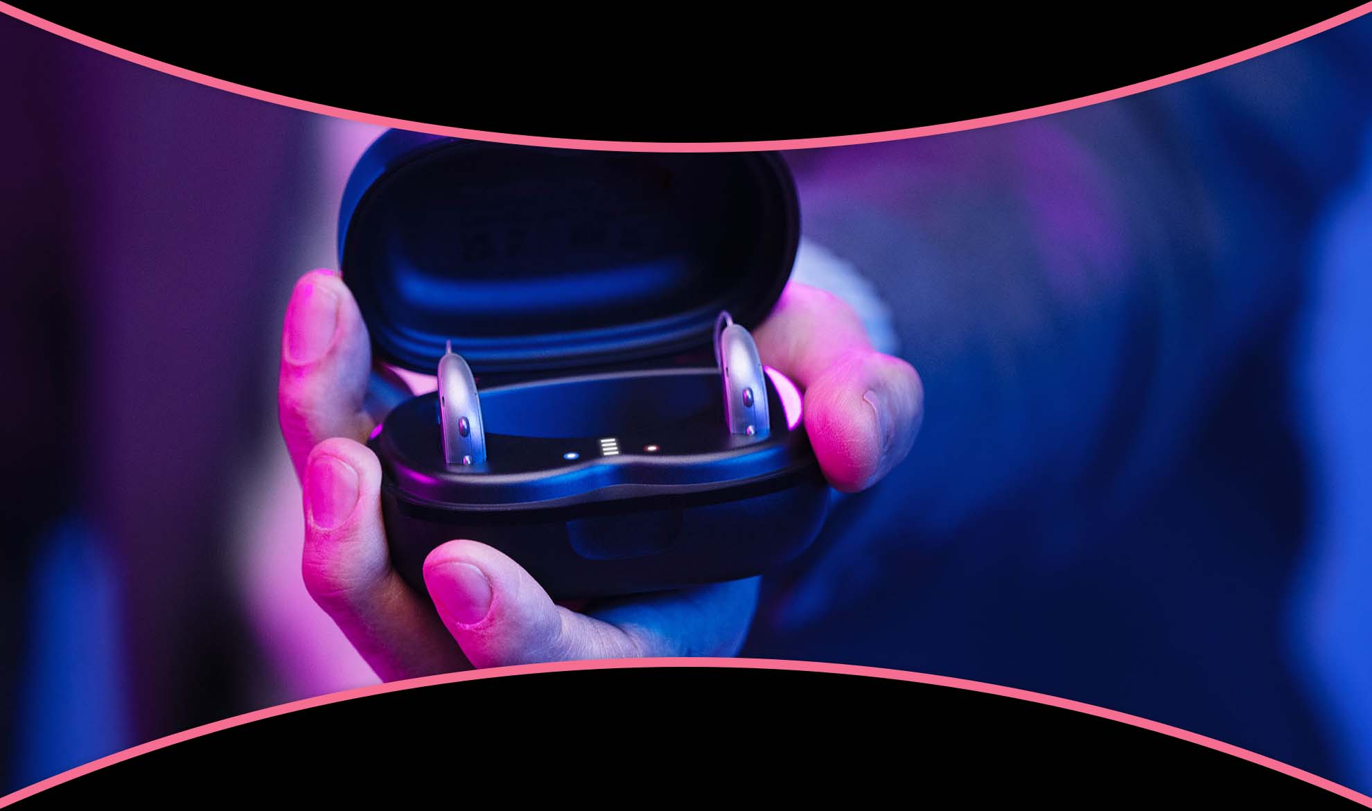 A hand holding an open charger with a pair of RIC hearing aids in it.